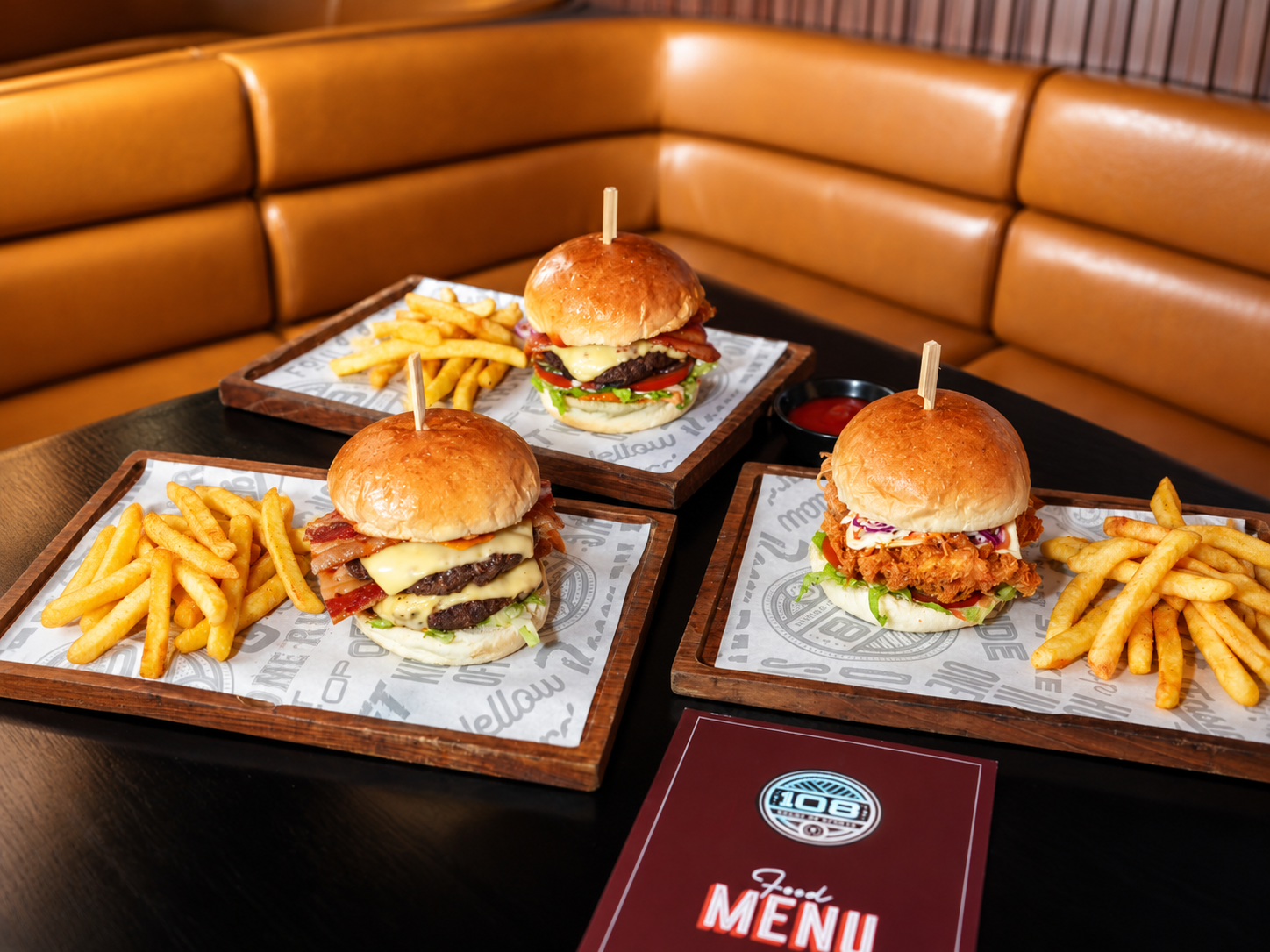 Three gourmet burgers served with fries in a cozy diner booth.
